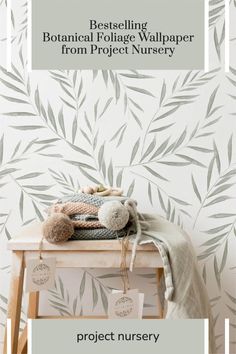 a white table topped with a stuffed animal next to a wallpaper covered in leaves