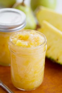 two jars filled with fruit sitting on top of a wooden table next to an apple