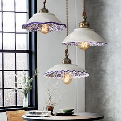 three lamps hanging from the ceiling above a table with a bowl on it and a vase in front