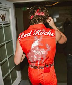 a woman in an orange jumpsuit is talking on her cell phone while wearing a red rock's vest