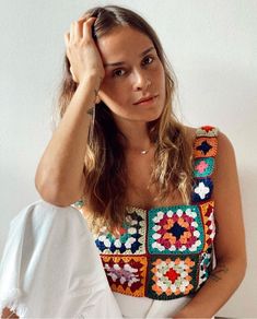 a woman sitting on top of a bed next to a white wall wearing a colorful shirt