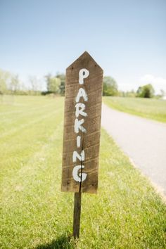 a wooden sign sitting on the side of a road next to a lush green field