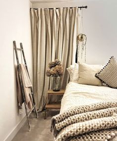 a bedroom with white walls and neutral colored bedding, window curtains, and decorative items