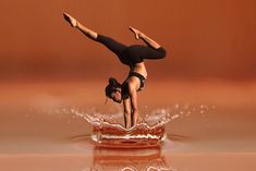 a woman doing a handstand on top of a body of water with her feet in the air