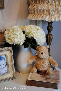 a teddy bear sitting on a table next to a vase with flowers and a photo