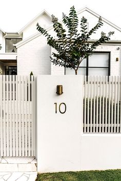 a house with a white fence and number 10 on the front gate, next to a small tree