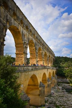 people are standing on the side of an old stone bridge over a river with many arches