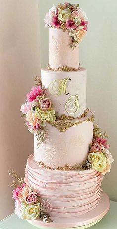 a three tiered wedding cake with pink and gold flowers on the top, sitting on a table