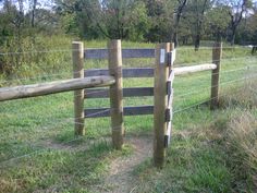 a wooden fence in the middle of a grassy field with trees and bushes behind it