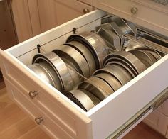 an open drawer in a kitchen filled with lots of silver dishes and pans on top of each other