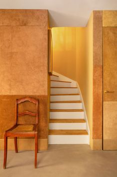 a wooden chair sitting in front of a stair case next to a wall with yellow walls