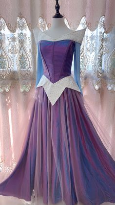 a purple and blue dress is on display in front of a pink curtain with white trim