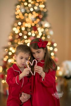 two children in red pajamas are holding heart shaped candy canes near a christmas tree