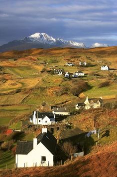 a small village on the side of a hill with snow capped mountains in the background