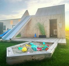 there is a sandbox with toys in it and a slide on the grass next to it