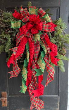 a red and green christmas wreath hanging on a door with pine cones, evergreens and ribbons