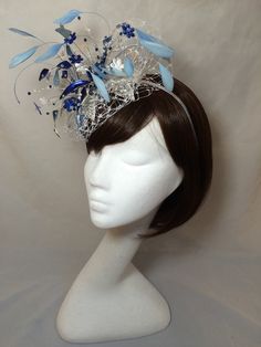 A stunning made to order blue Fascinator combines glass flower petals, leaves and knitted mesh wire work. This piece combines specialized techniques which blend together in a stunning display to create a showstopping piece which will add instant impact to any outfit. This design is set onto a band which is fairly invisible due to the main design coverage of the band and also the soft covering of veiling. The design is completed with a scattering of coque feather and stems of crystals. As with al Light Blue Headpiece For Royal Ascot Party, Blue Feathered Headpiece For Party, Handmade Structured Crown Fascinator For Party, Blue Feathered Wedding Fascinator, Blue Feathered Wedding Costume Hat, Blue Fascinator With Handmade Flowers For Kentucky Derby, Blue Handmade Flowers Fascinator For Races, Light Blue Headpiece For Kentucky Derby Party, Blue Wedding Costume Hat With Feathers