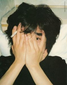 a young man covers his face with his hands while laying on a bed in front of him