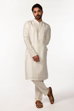 Ivory full sleeve kurta with mirror embroidered sleeve hem and mandarin collared neckline. Paired with pant pyjama.
Components: 2
Pattern: Embroidery
Type Of Work: Mirror
Neckline: Mandarin collar
Sleeve Type: Full sleeves
Fabric: Kurta: Bam Silk, Pant Pyjama: Cotton Silk
Color: Ivory
Other Details: 
Front concealed button placket
Occasion: Mehendi and Puja - Aza Fashions Mens Designer Kurta, Full Sleeve Kurta, Embroidery Mirror, Silk Pant, Pattern Embroidery, Mirror Set, Silk Embroidery, Full Sleeves, Color Ivory