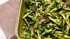 broccoli and other vegetables are in a green dish on a tablecloth next to a fork