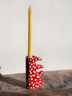 a red and white polka dot candle holder with a single yellow candle in the middle