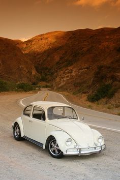 an old vw bug is parked on the side of the road in front of mountains