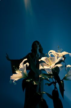 a woman standing next to a white flower on top of a blue sky filled with light