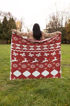 a woman is holding up a red and white blanket in the grass with snowflakes on it