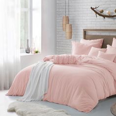 a bed with pink sheets and pillows in a room next to a white brick wall