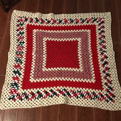 a red and white crocheted blanket sitting on top of a wooden floor