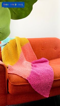 an orange couch with a pink and yellow blanket on it, next to a potted plant