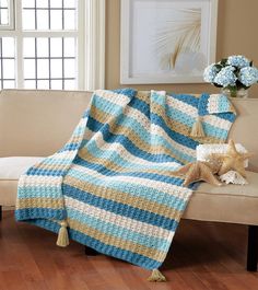 a blue and yellow blanket sitting on top of a couch next to a vase with flowers