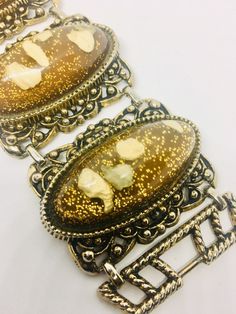 Fabulous vintage extra wide Lucite confetti glitter bracelet with imbedded pebbles. Long lucite cabochons set in ornate antiqued gold tone metal settings. Brown/copper and gold glitter color perfect for fall. Bracelet is in excellent vintage condition with minimal age appropriate wear... if any. It measures 7 1/2 inches long by 2 inches wide. Clasp secure.   Thanks for looking. Jeweled Gold Brass Bracelet, Gold Jeweled Brass Bracelet, Vintage Resin Jewelry For Party, Vintage Resin Jewelry For Parties, Antique Gold Bracelet With Antique Finish, Formal Gold Bracelets With Antique Finish, Bohemian Gold Oval Bracelets, Gold Oval Bohemian Bracelets, Formal Gold Bracelet With Antique Finish