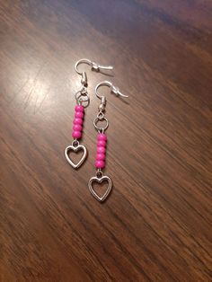 two pink beaded heart earrings sitting on top of a wooden table