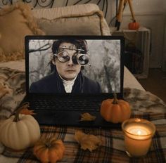 a laptop computer sitting on top of a bed next to pumpkins and candles in front of it