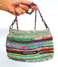 a hand holding a multicolored crocheted purse with black handles and metal chain