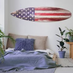 an american flag surfboard hanging on the wall above a bed with pillows and blankets