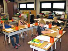 children sitting at desks in a classroom with books and pencils on their laps