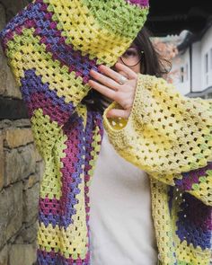 a woman is covering her face with a crochet shawl