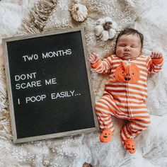 a baby laying next to a sign that says two months don't scare me i poop easily