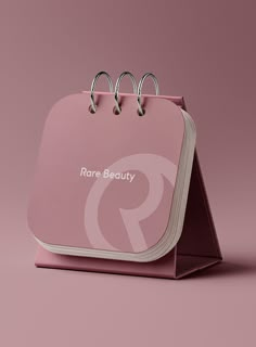 a pink paper bag with three rings on the front and two sides that say rare beauty