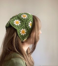 a woman wearing a green crochet hat with white flowers on the front and yellow centers