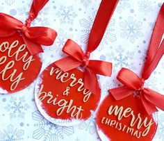 three christmas ornaments with red ribbon and merry lettering on the top one is hanging from a bow