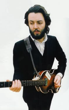 a man with long hair and beard holding an electric guitar in his right hand while wearing a suit