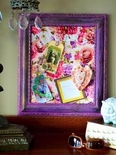 a purple frame with pink flowers and pictures on it next to some books, sunglasses and a figurine