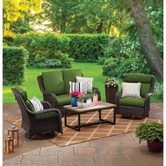 an outdoor patio furniture set with blue cushions and pillows on a rug in front of a tree