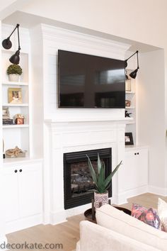 a living room with white furniture and a flat screen tv mounted on the wall above a fireplace