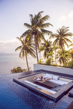 an outdoor living area with palm trees and water in the foreground, overlooking the ocean