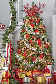 a decorated christmas tree with presents under the banister and stairs in front of it