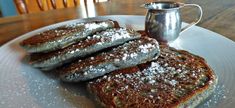 four pieces of french toast with powdered sugar on them and a silver coffee pot